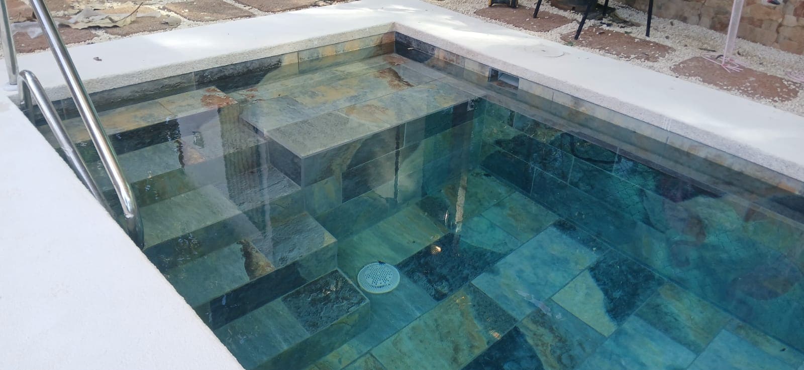 Square plunge pool with dark travertine coping and woodland backdrop
